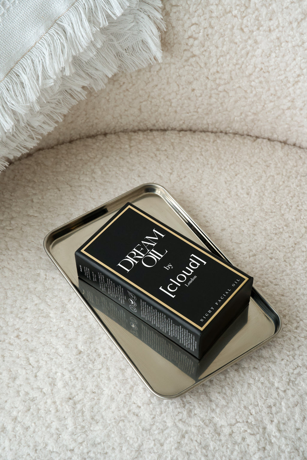 Photo of a Dream Oil box lying in a shinny metal tray sat on a soft luxury texture seat. 