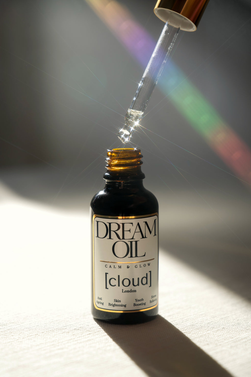 A pipette hovering above a bottle of Dream Oil, the sunlight is shining off the oil showing how lightweight it is. 